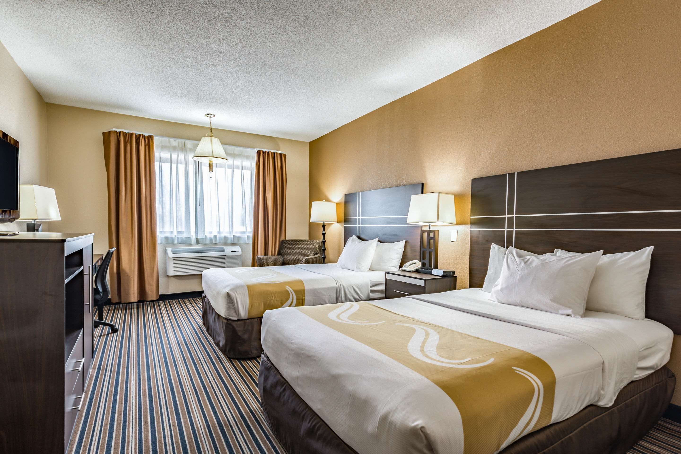 A hotel room with two beds, a desk, a chair, a TV, and a window with curtains.