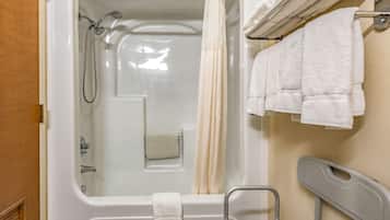 A bathroom with a bathtub, a shower, a towel rack with towels, and a grab bar.