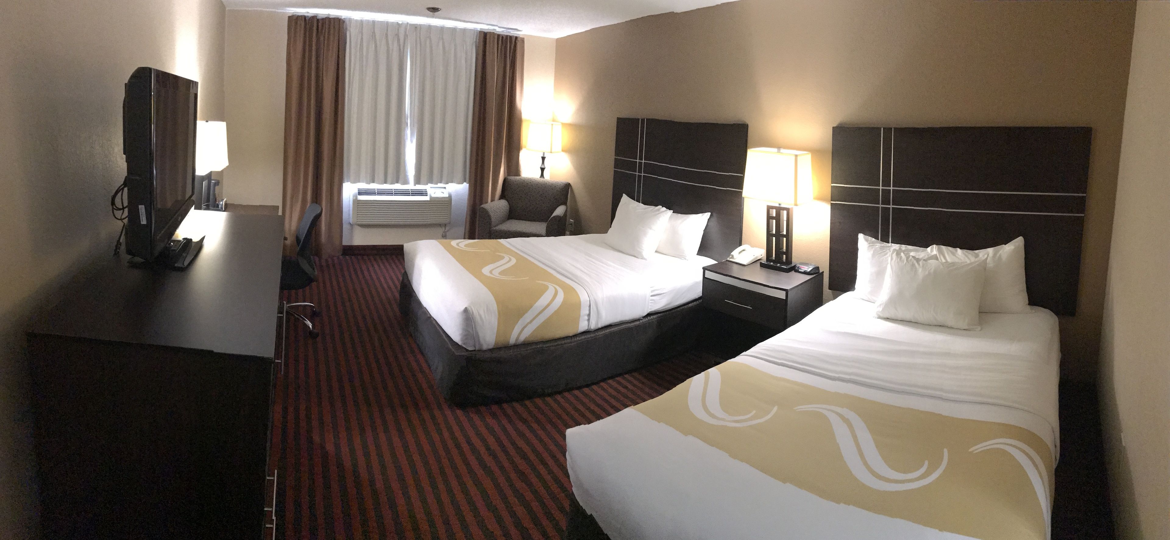 A hotel room with two beds, a desk with a computer, a chair, and a lamp.
