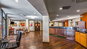 A spacious lobby with a reception desk, a seating area with a table and chairs, and a wooden floor.
