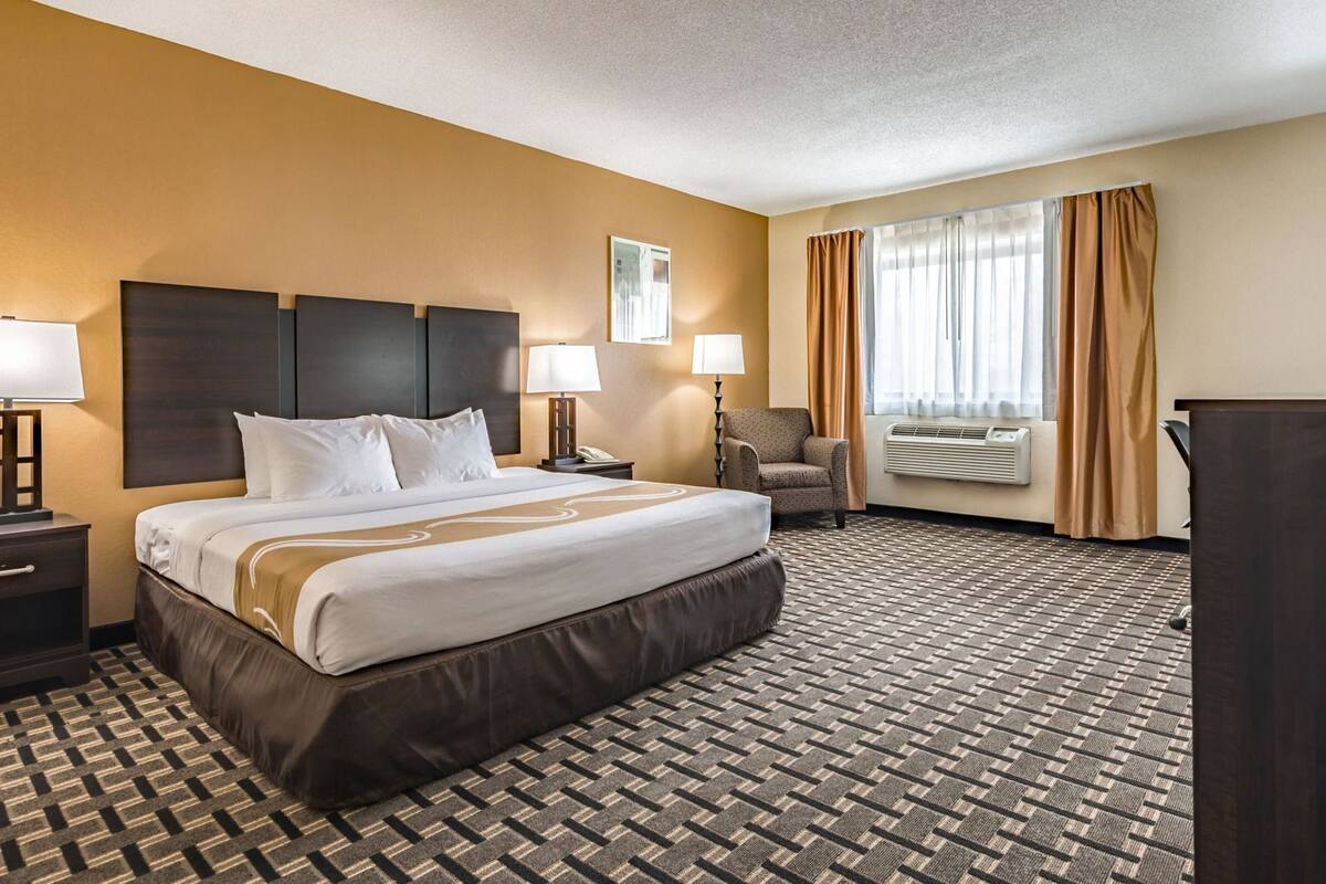A hotel room with a large bed, two bedside tables, a chair, a desk, and a window with curtains.
