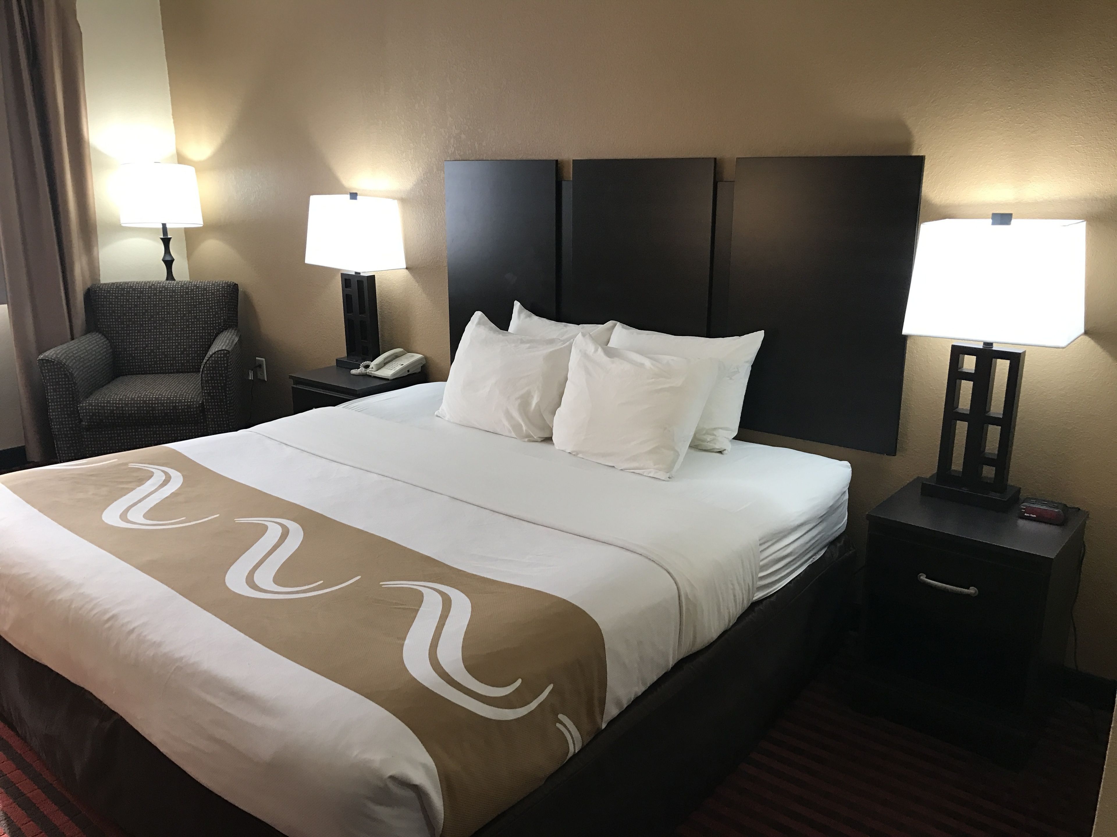 Une chambre d’hôtel avec un grand lit, deux tables de chevet, une chaise et deux lampes.