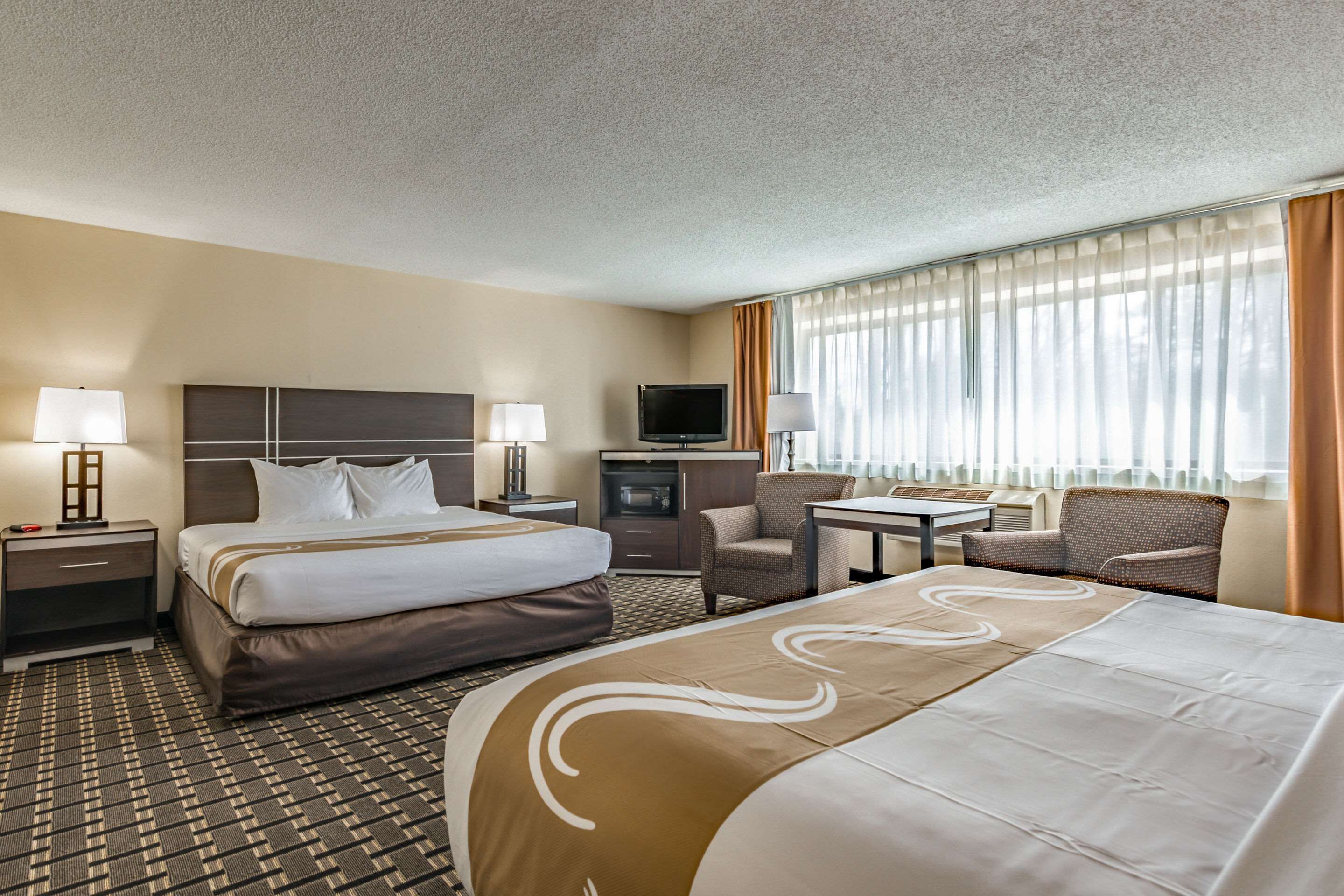 Ein Hotelzimmer mit einem großen Bett, einem Schreibtisch, einem Stuhl, einem Fernseher und einem Fenster mit Vorhängen.