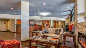 A spacious lobby with a sofa, coffee table, and a fireplace. There is a reception desk in the background. - Quality Inn Schenectady - Albany (Schenectady)