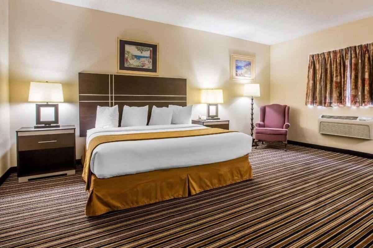 A hotel room with a large bed, two bedside tables with lamps, a chair, and a window with curtains.