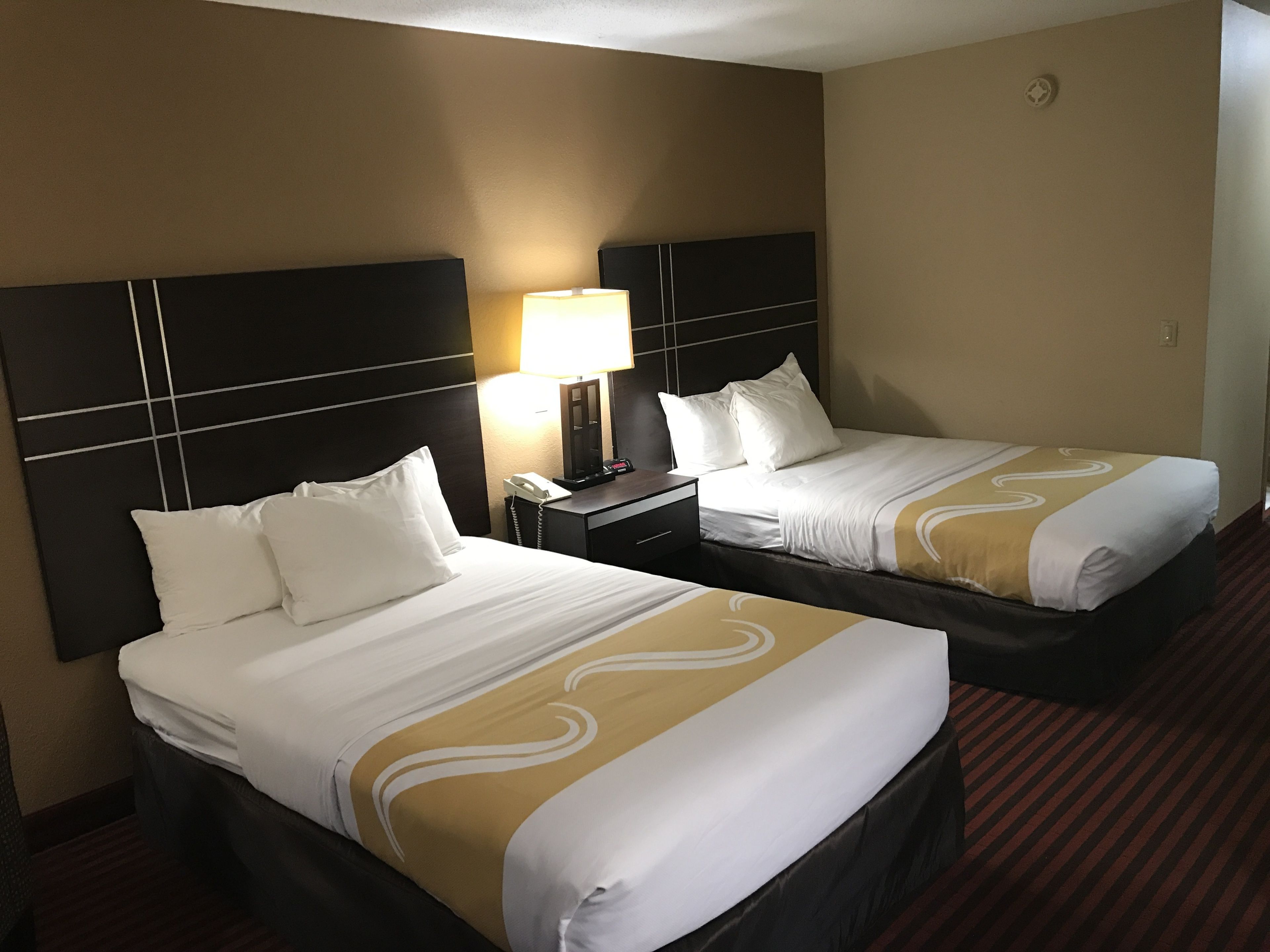 A hotel room with two beds, each with a headboard, a bedside table with a lamp, and a telephone.