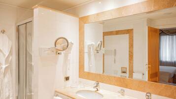 A modern bathroom with a large mirror, two sinks, a glass shower enclosure, and a towel rack.