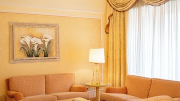 A hotel room with two patterned sofas, a small round table with a lamp, and a framed floral painting on the wall.