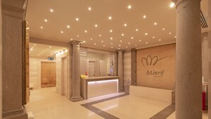 A hotel reception area with a marble reception desk, a wooden wall with the hotel name, and a clean, modern design. - Royal Hotel Carlton (Bologna)