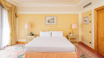 A hotel room with a large bed, two bedside tables, a nightstand, a wooden door, and a patterned carpet.