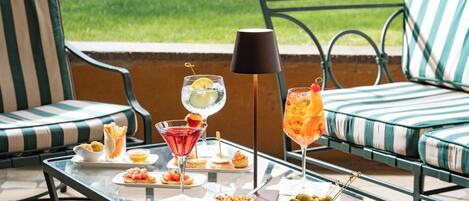 A glass table with food and drinks, green striped chairs, and a lamp.