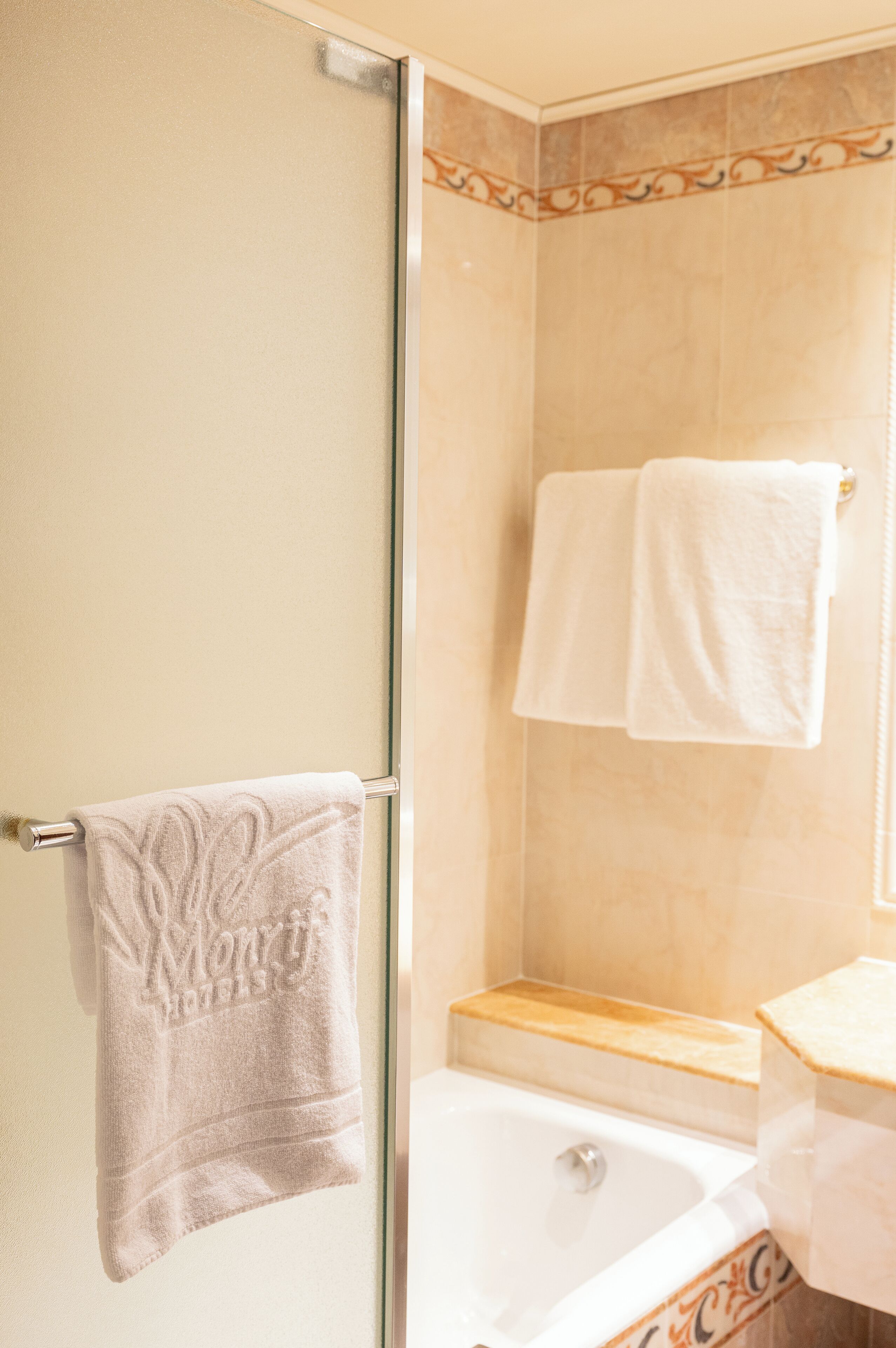 Un bagno con doccia in vetro, una vasca e due asciugamani bianchi appesi a un portascopevoli.