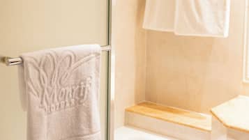 Un baño con mampara de vidrio, bañera y dos toallas blancas colgadas en un perchero.