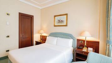 Un cuarto de hotel con una cama grande, dos mesitas de noche con lámparas, una puerta de madera, un cuadro en la pared y una ventana con cortinas.