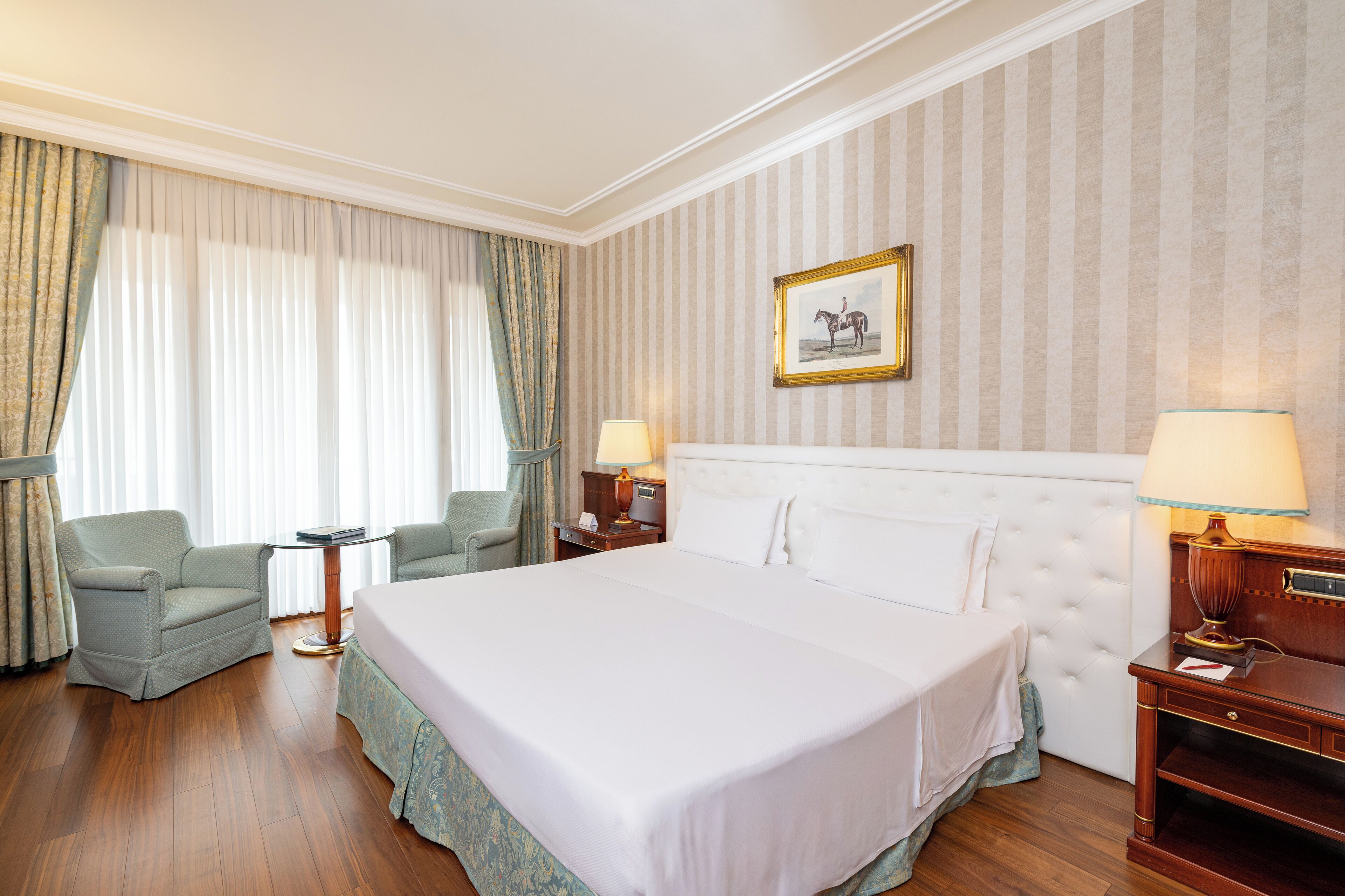 A hotel room with a large bed, two bedside tables with lamps, a chair, and curtains.