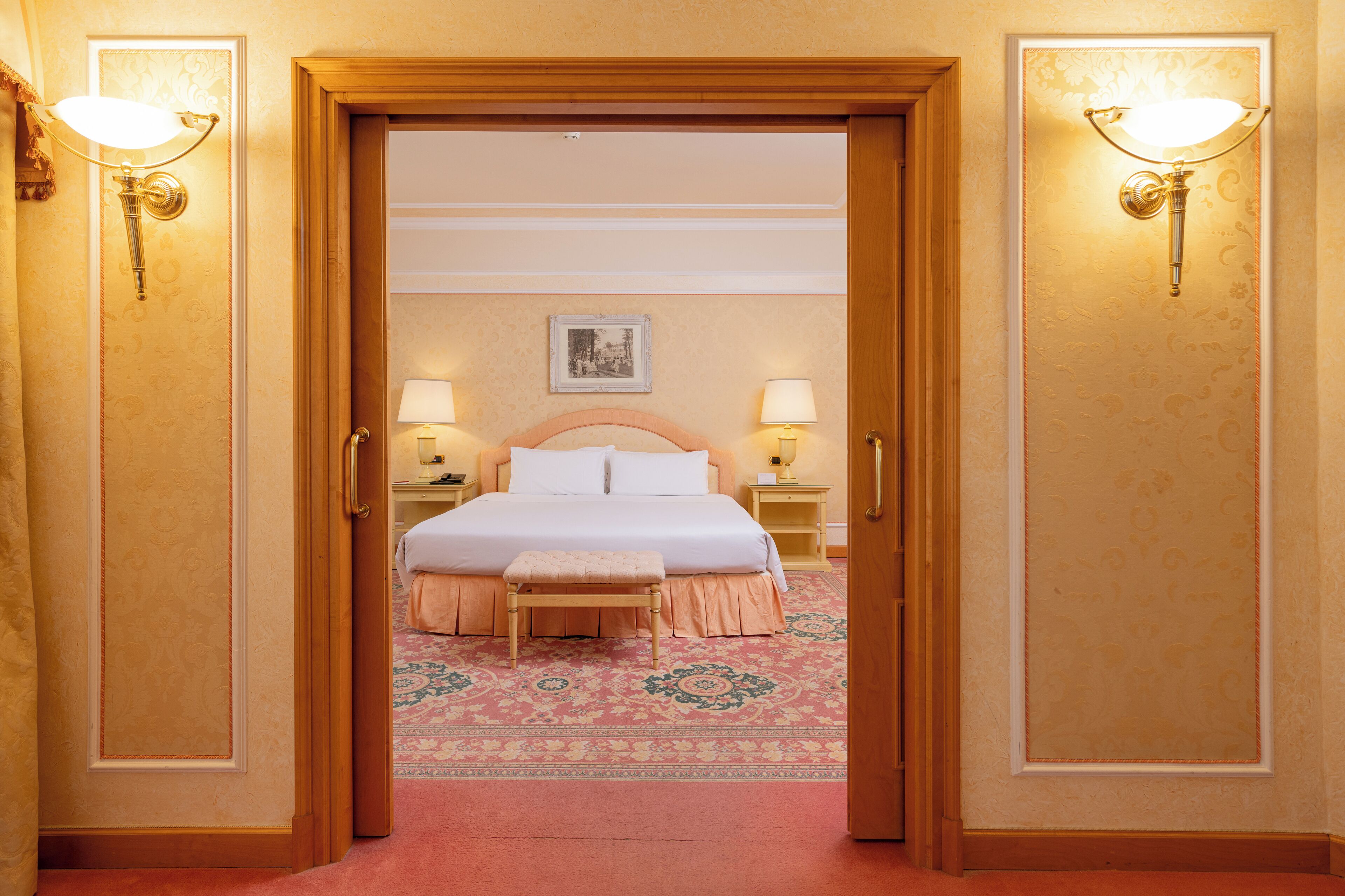 A hotel room with a bed, two bedside lamps, a nightstand, and a small table.