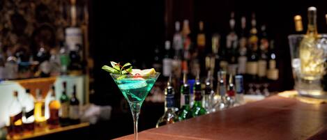 Un bar con una copa de martini que contiene un cóctel azul, una rodaja de limón y una guarnición verde.