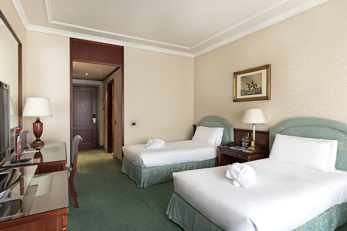 Une chambre d’hôtel avec deux lits simples, un bureau avec une lampe, une chaise et un téléviseur.