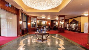 A lobby with a marble floor, a central table with decorative items, and a large chandelier. - Royal Hotel Carlton (Bologna)