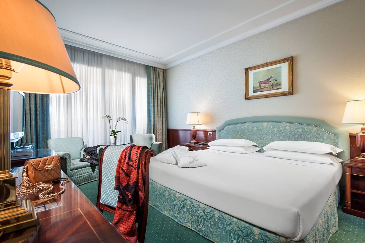 Une chambre d’hôtel avec un grand lit, un bureau avec une lampe, une chaise et un tableau au mur.