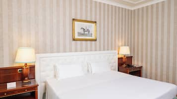 Une chambre d’hôtel avec un grand lit, deux tables de chevet avec des lampes, un tableau encadré au mur et un papier peint à rayures.