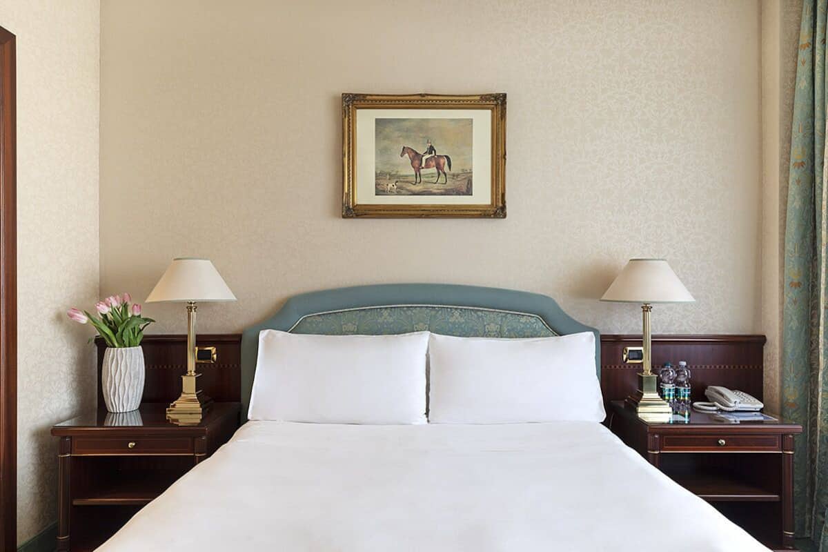 Une chambre d’hôtel avec un grand lit, deux tables de chevet avec des lampes, un tableau encadré au mur et un vase de fleurs posé sur l’une des tables.