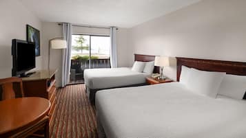 Een hotelkamer met twee bedden, een bureau met een televisie, een stoel en uitzicht op de omgeving.