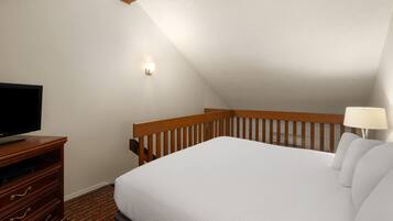 A bedroom with a bed, a TV on a wooden stand, a nightstand, a lamp, and a sloped ceiling.
