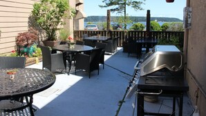 Eine Terrasse im Freien mit runden Tischen und Stühlen, einem Grill und einem hängenden Blumentopf.