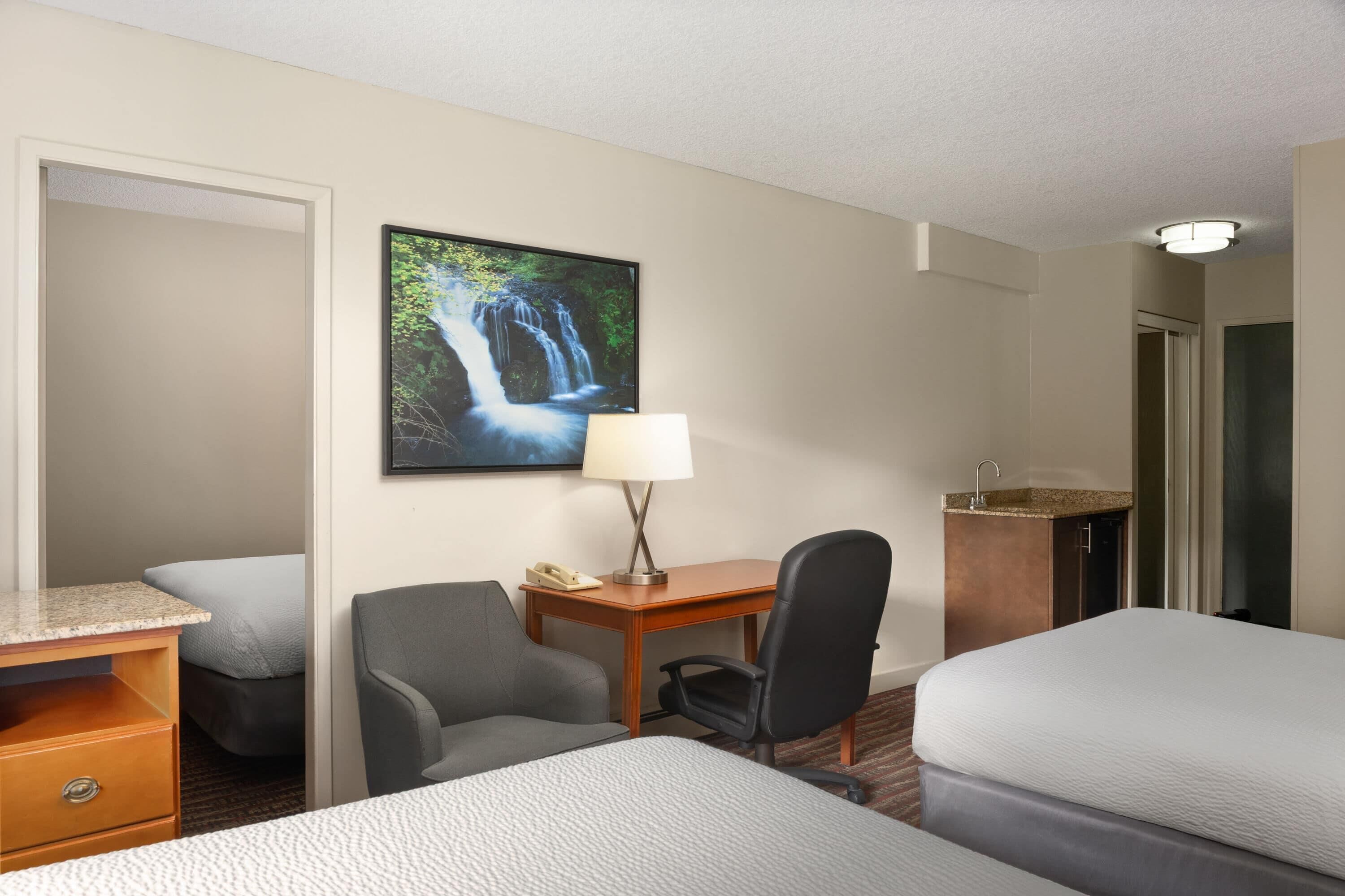 Habitación de hotel con dos camas, un escritorio, una silla, un teléfono y un cuadro de una cascada.