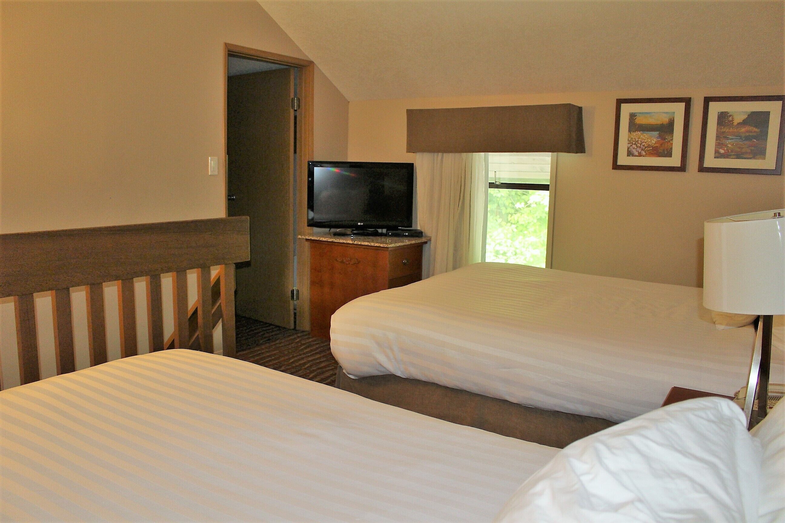 Habitación de hotel con dos camas, un televisor sobre un soporte de madera y una ventana con cortinas.