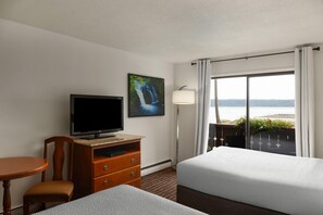 Une chambre d’hôtel équipée d’une télévision, d’un bureau, d’une chaise, de deux lits, d’une fenêtre avec des rideaux et offrant une vue sur la mer.