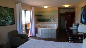 Ein Hotelzimmer mit einem großen Bett, einem Badezimmer mit Badewanne, einem Sessel und einem Schreibtisch mit Lampe.
