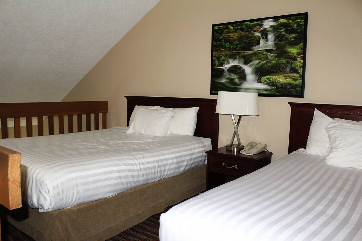 Ein Hotelzimmer mit zwei Betten, einem Nachttisch mit Lampe und einem Wandbild mit einem Wasserfall.