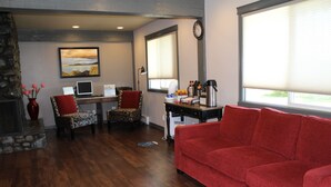Ein Wohnzimmer mit rotem Sofa, gemusterten Sesseln, einem Kamin, einem Schreibtisch mit Computer und einem großen Fenster mit Jalousien.