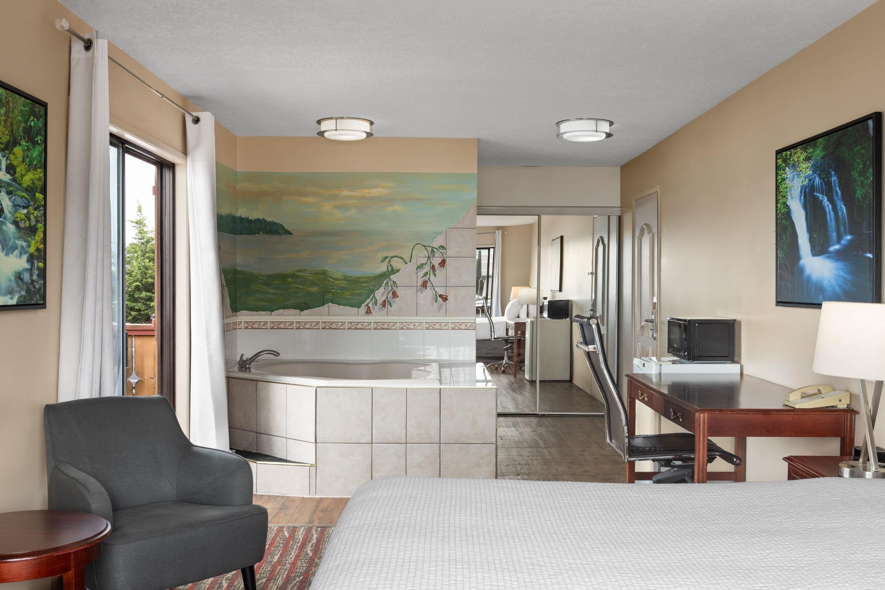 A hotel room with a bed, a desk, a chair, a bathroom with a bathtub, and a painting of a waterfall.