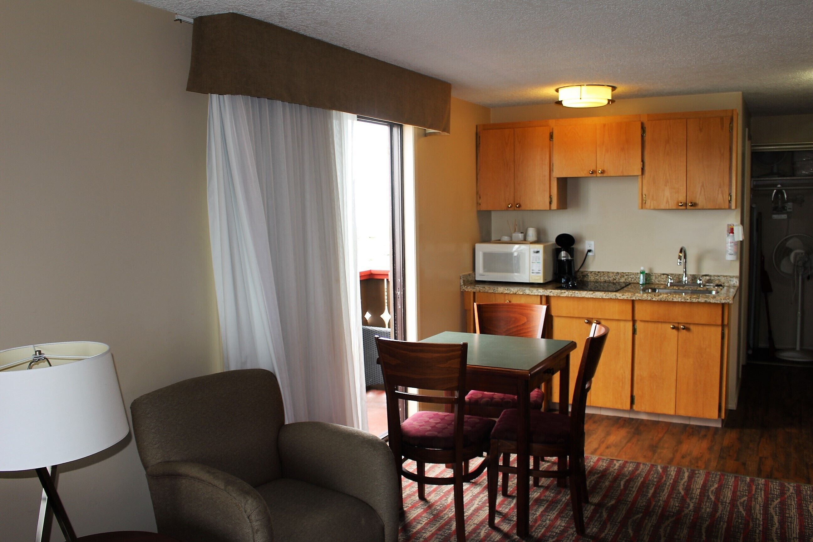 A compact hotel room with a dining area, a kitchenette, and a large window with curtains.