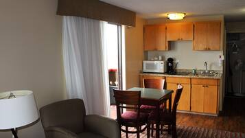 A compact hotel room with a dining area, a kitchenette, and a large window with curtains.