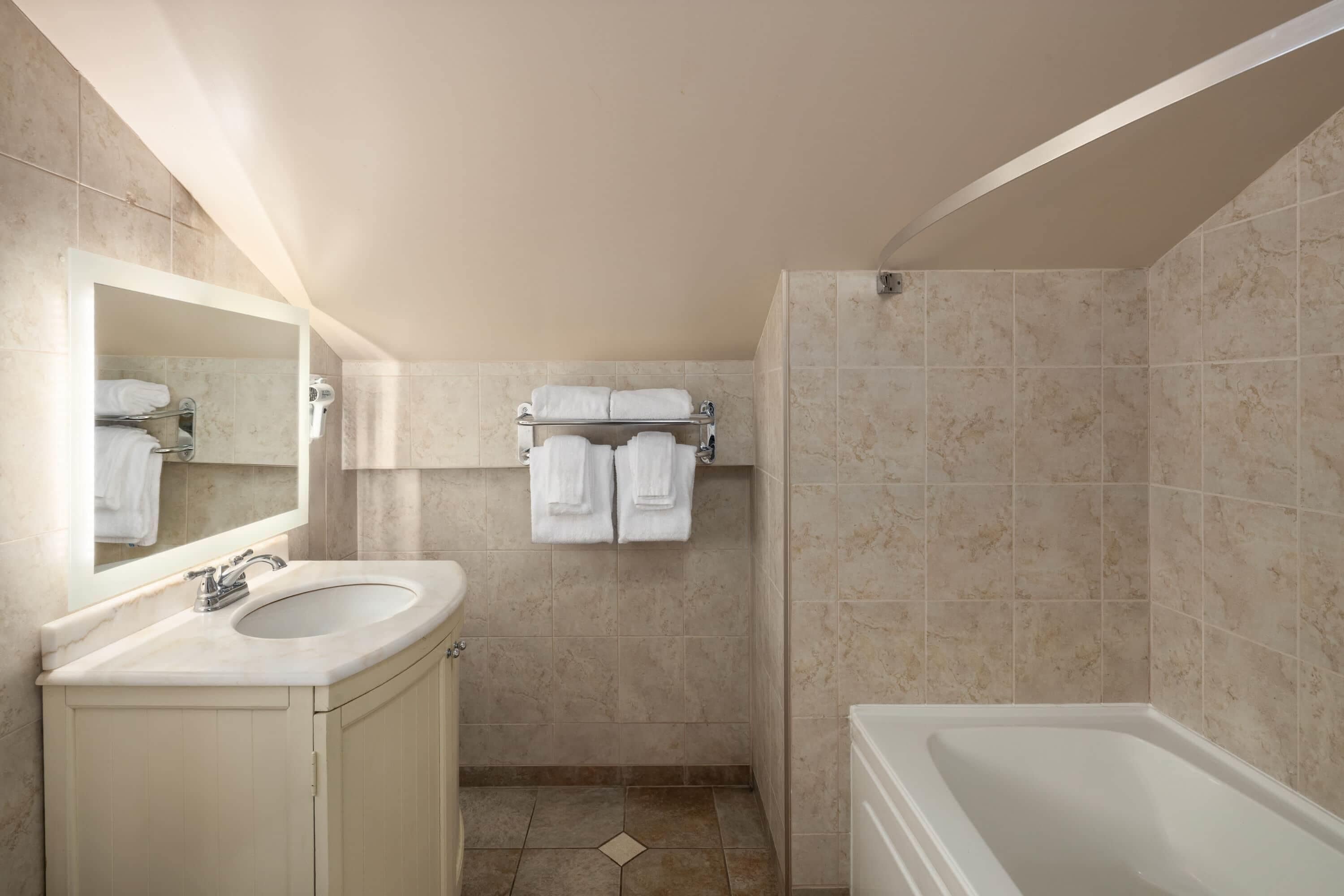 Un baño con lavamanos, espejo, toallero y bañera.