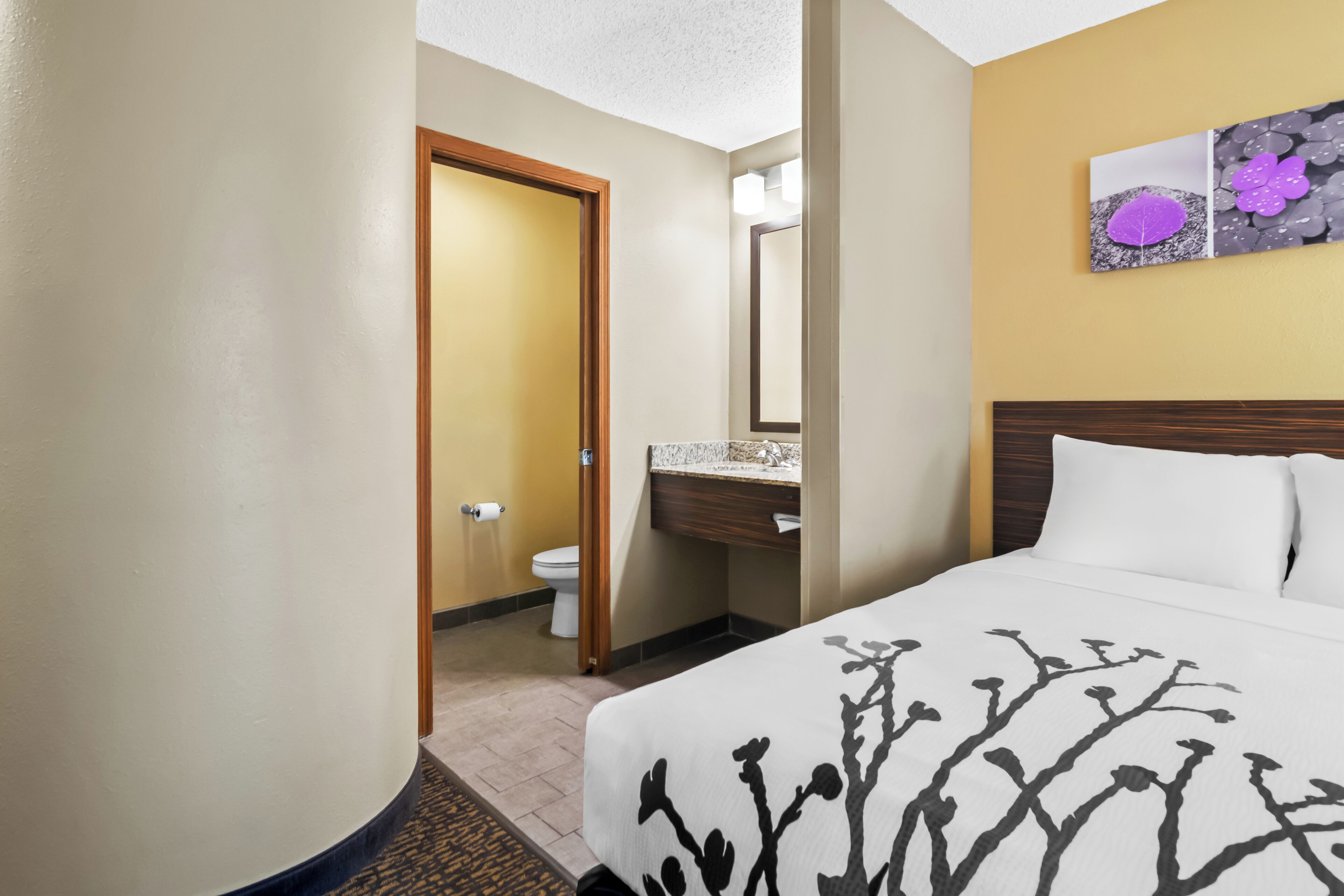 A hotel room with a bed, a bathroom, and a painting on the wall.