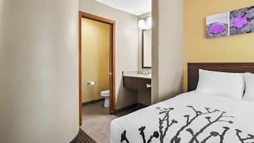 A hotel room with a bed, a bathroom, and a painting on the wall.