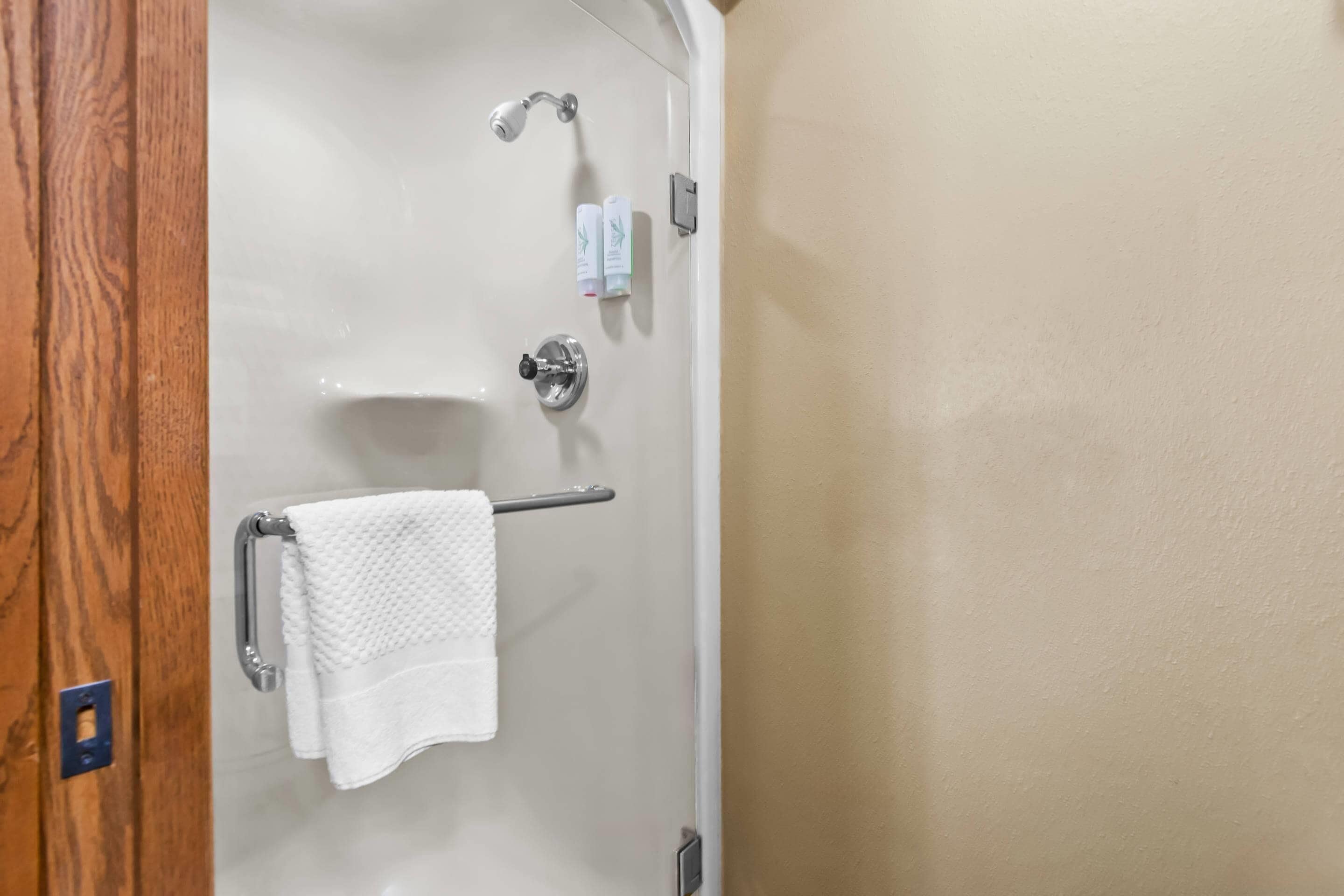 A bathroom with a glass-enclosed shower, a towel rack with a white towel, and two small bottles on the wall.