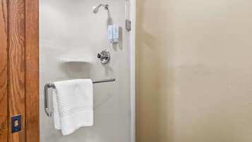 A bathroom with a glass-enclosed shower, a towel rack with a white towel, and two small bottles on the wall.