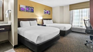 Habitación de hotel con dos camas, un escritorio, una silla, una lámpara y obras de arte en la pared.