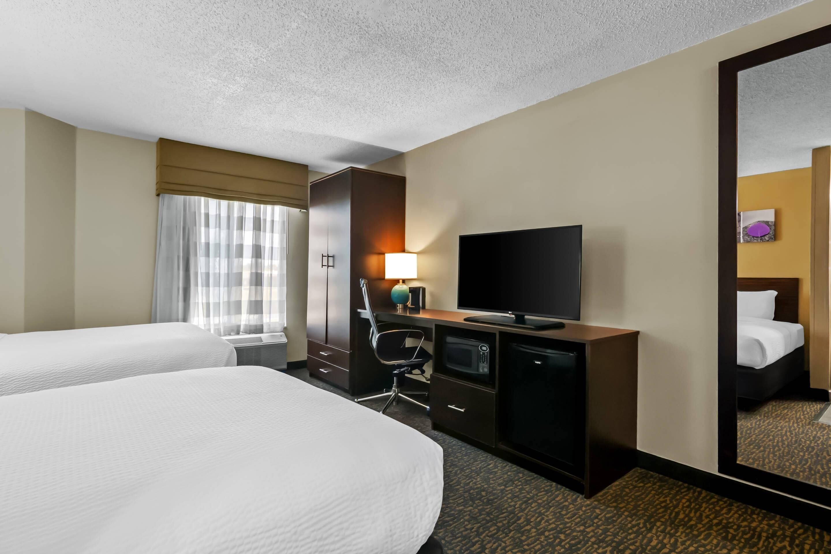 A hotel room with two beds, a television, a desk with a lamp, and a microwave.