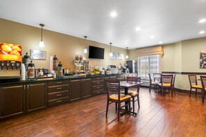 A modern kitchen with dark wooden cabinets, a central island, and a dining area with wooden chairs. - Sleep Inn Fayetteville North (Fayetteville)