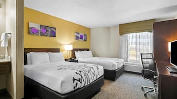 A hotel room with two beds, a desk, a chair, a TV, and artwork on the wall.