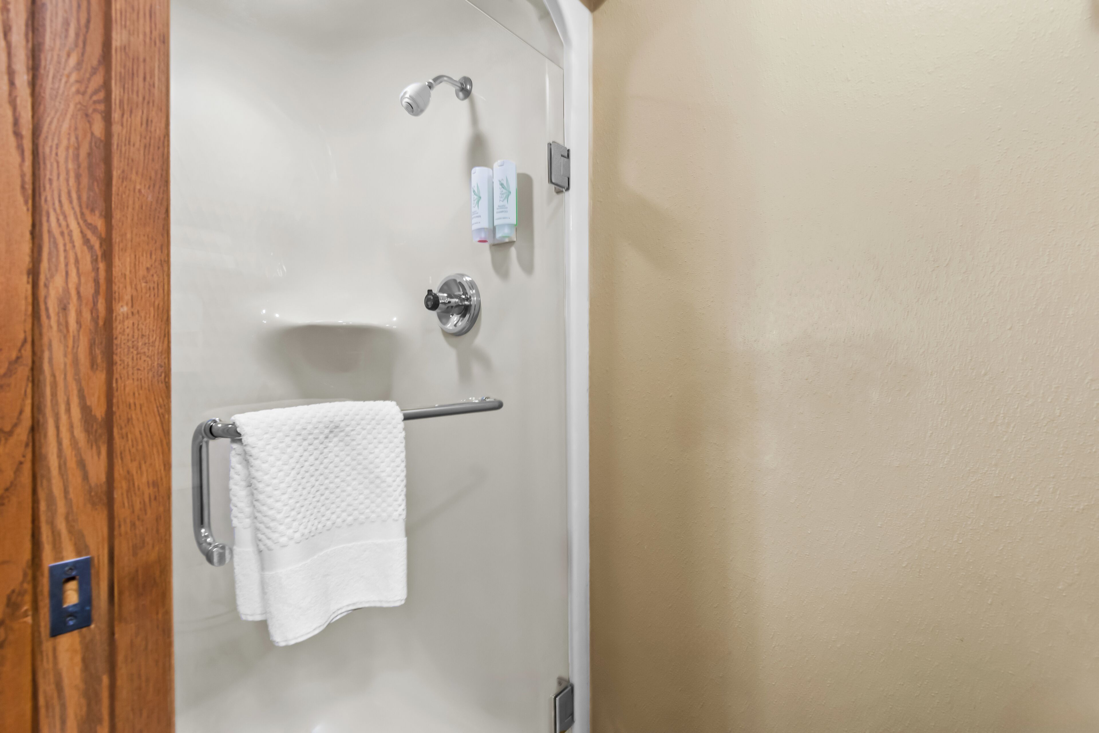 A bathroom with a white bathtub, a towel rack with a white towel, and two bottles of shampoo and conditioner on the wall.