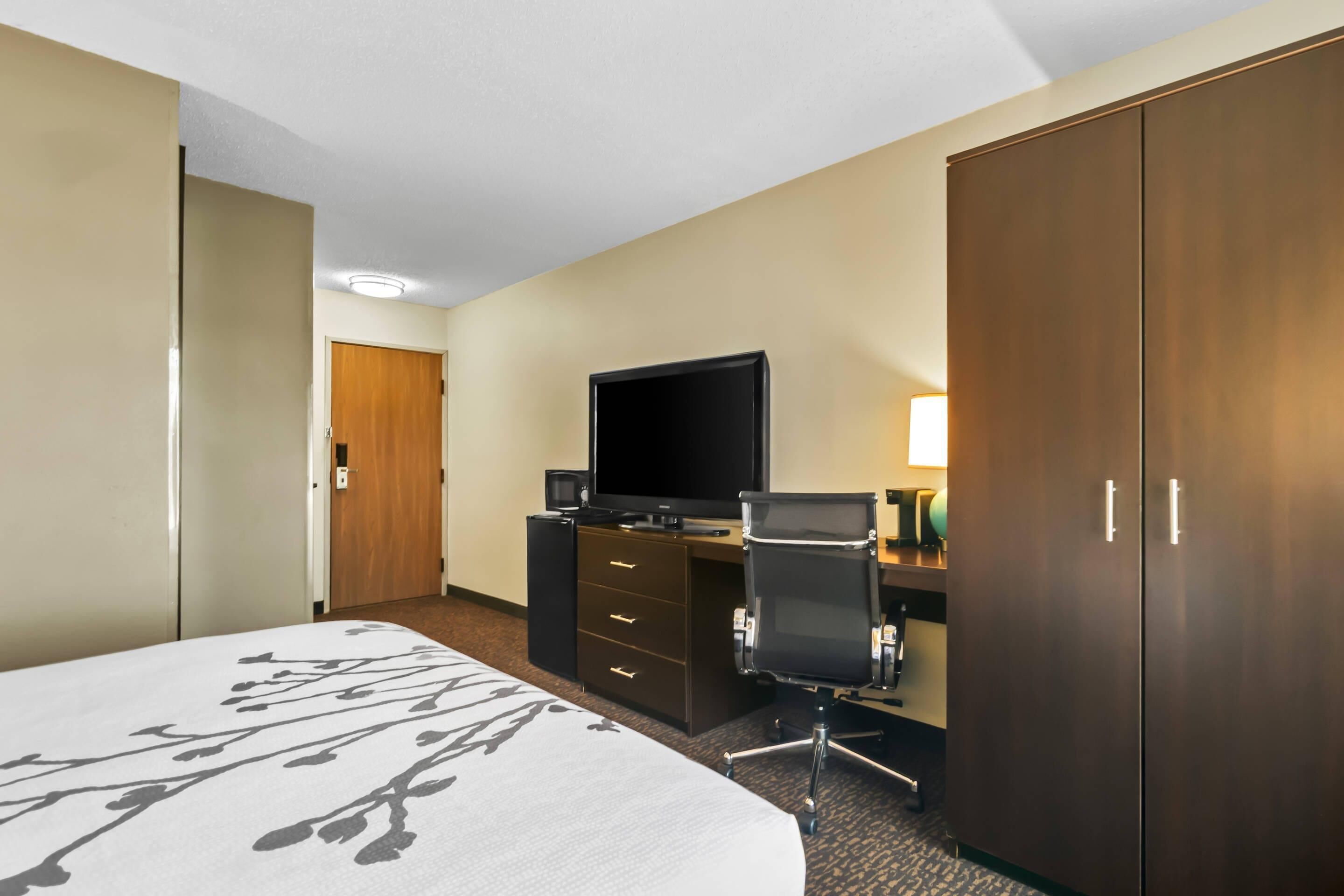 A hotel room with a bed, a desk with a computer, a television, and a wardrobe.