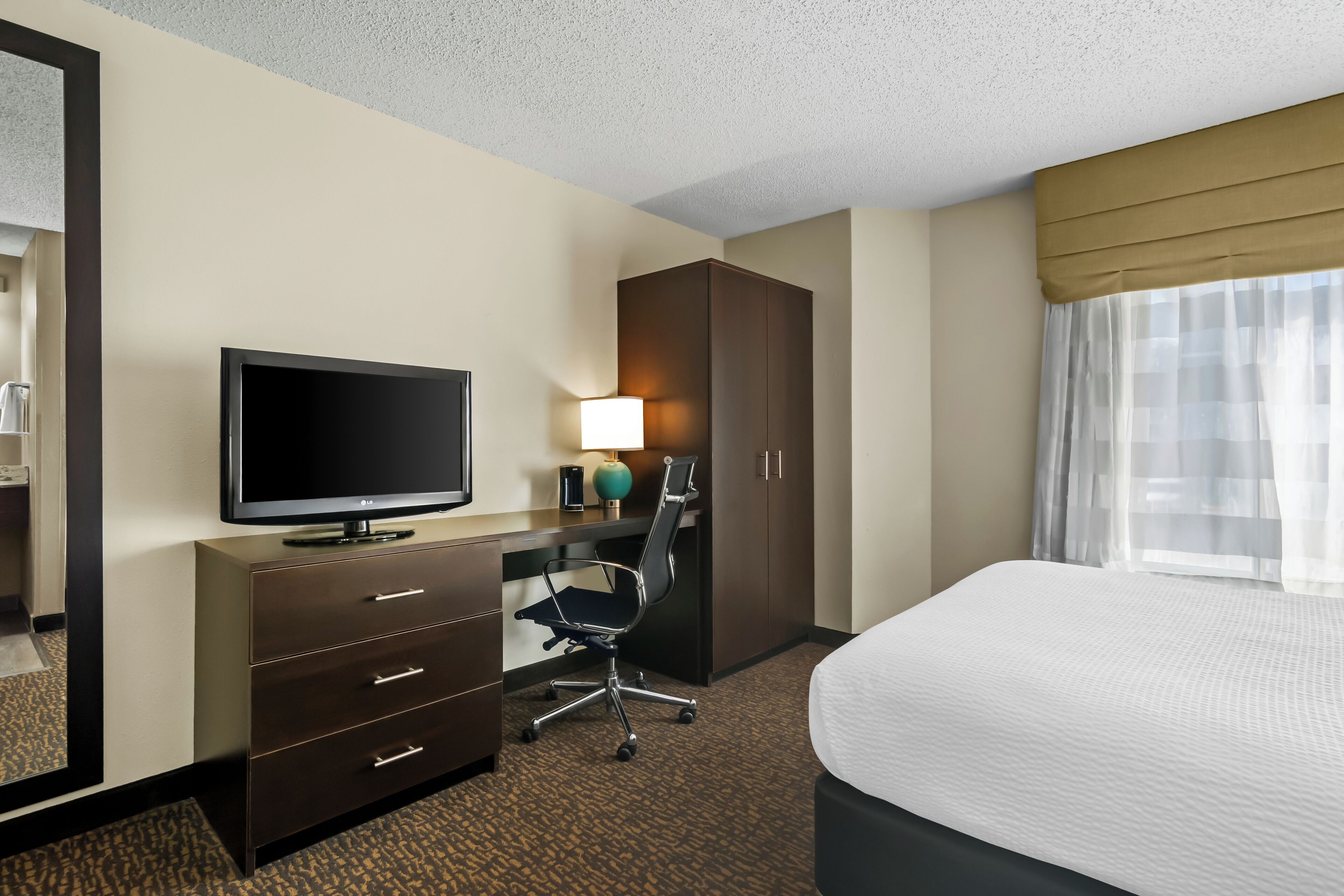 A hotel room with a bed, a desk with a computer, a TV, and a wardrobe.